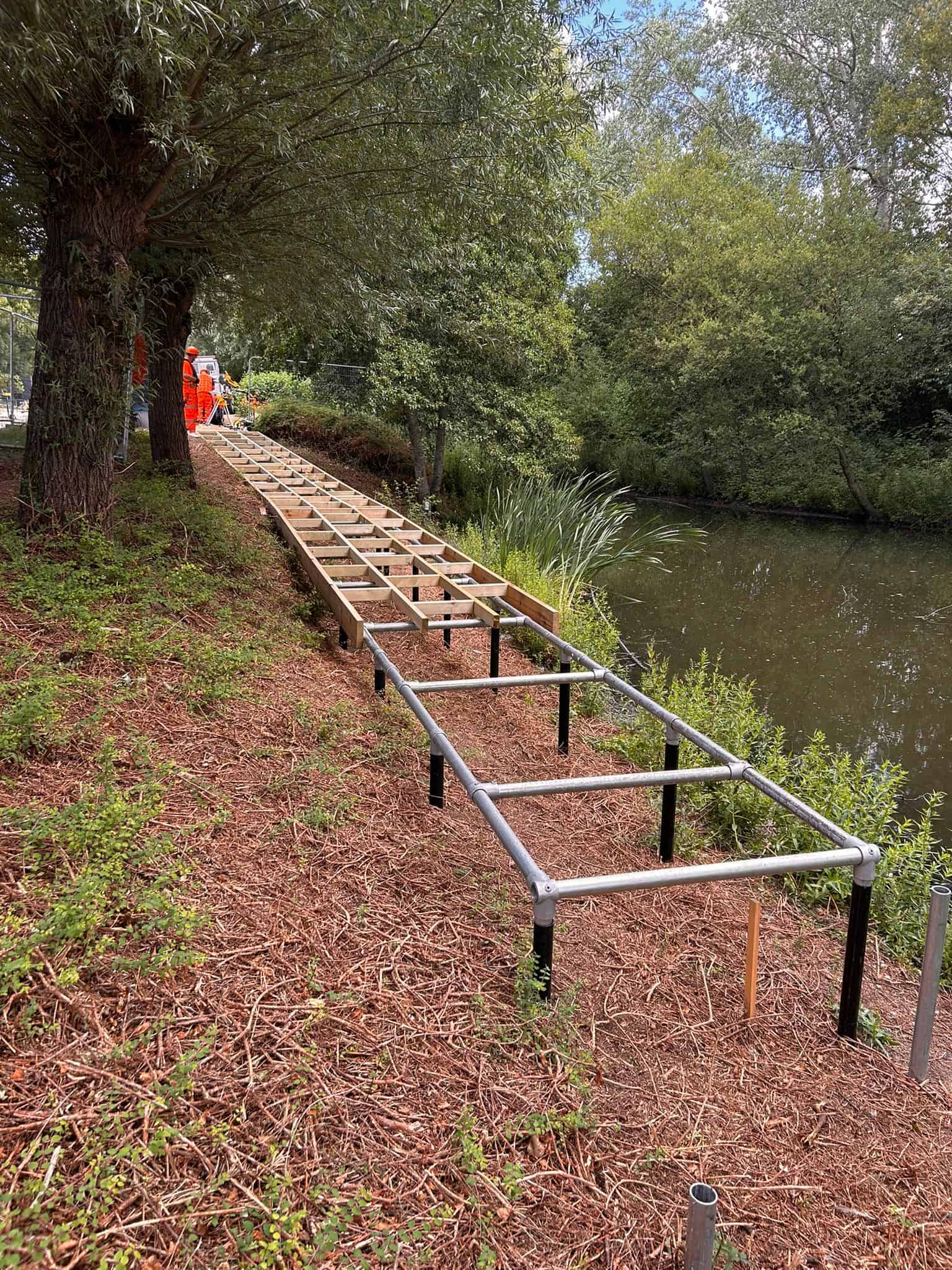 The supporting framework made from galvanised tubes running along the excavated path by the pond.