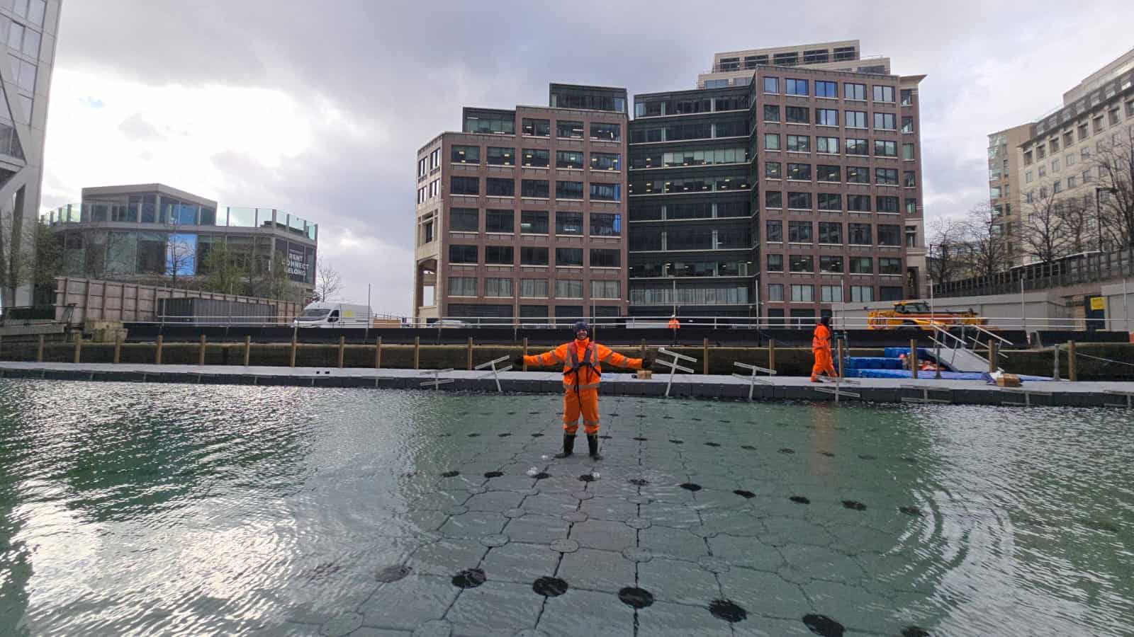 A WMS installer stands with his arms out in the middle of the Modular Cube pool floor as it sinks.